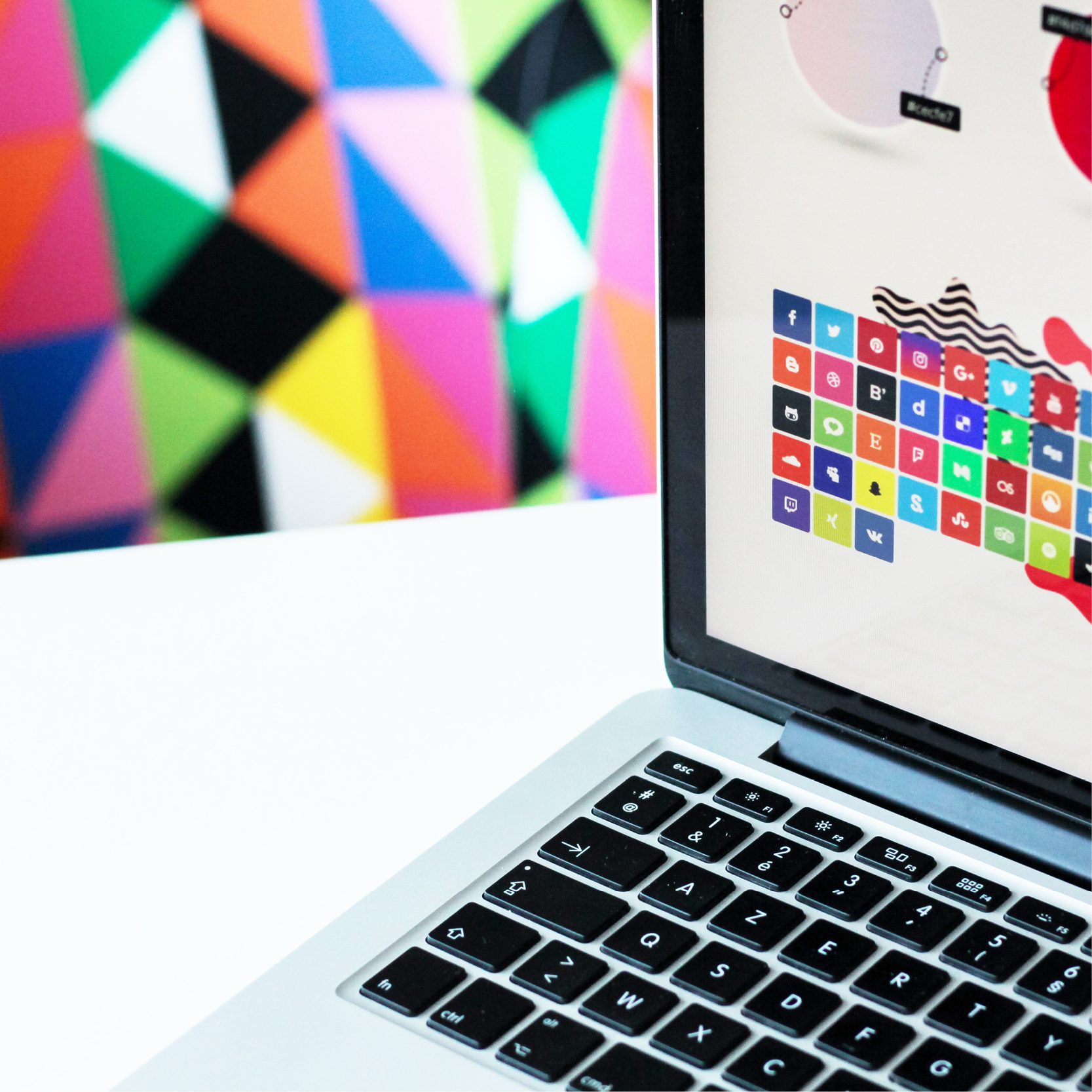 Picture of Macbook Laptop with social media icons on the screen and colourful shapes in the background