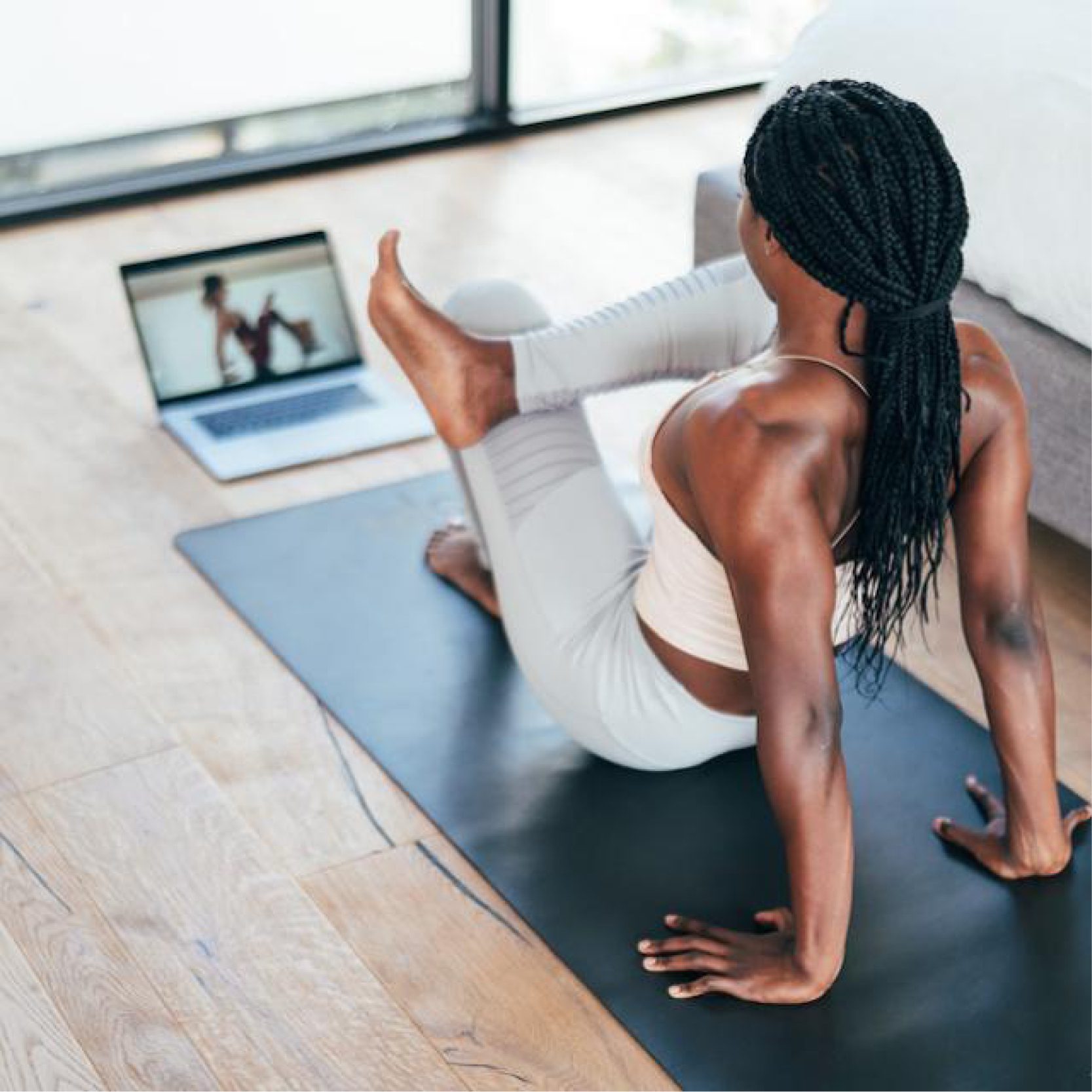 Woman in a yoga pose on a black yoga mat following an online instructor on her laptop